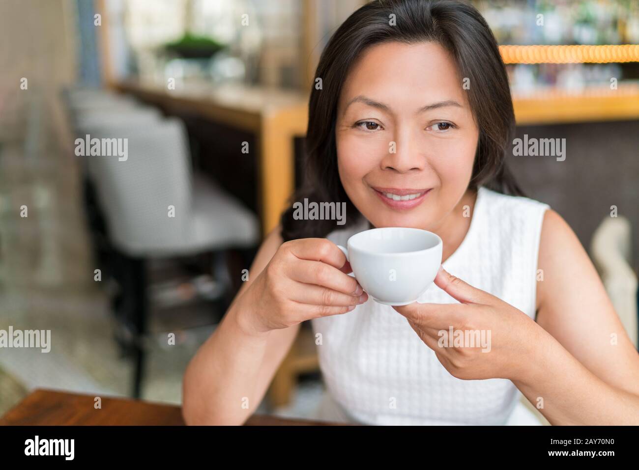 Donna asiatica matura bere inglese colazione tè rilassante al caffè. Signora cinese di mezza età che gode stile di vita della città, vita elegante. Foto Stock