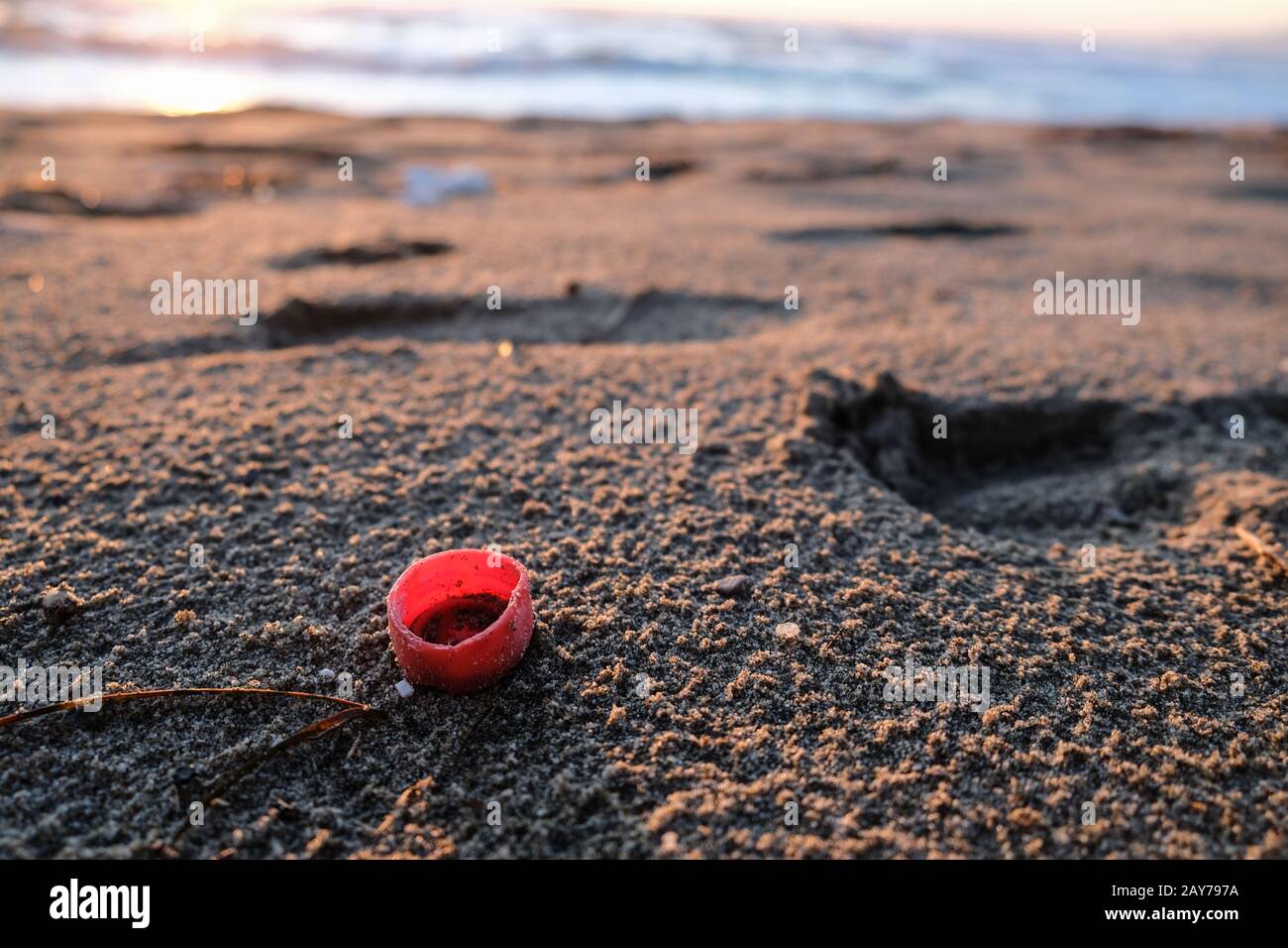 Tappo in plastica rossa sulla costa del mare al tramonto, ecosistema inquinato, microflastica Foto Stock