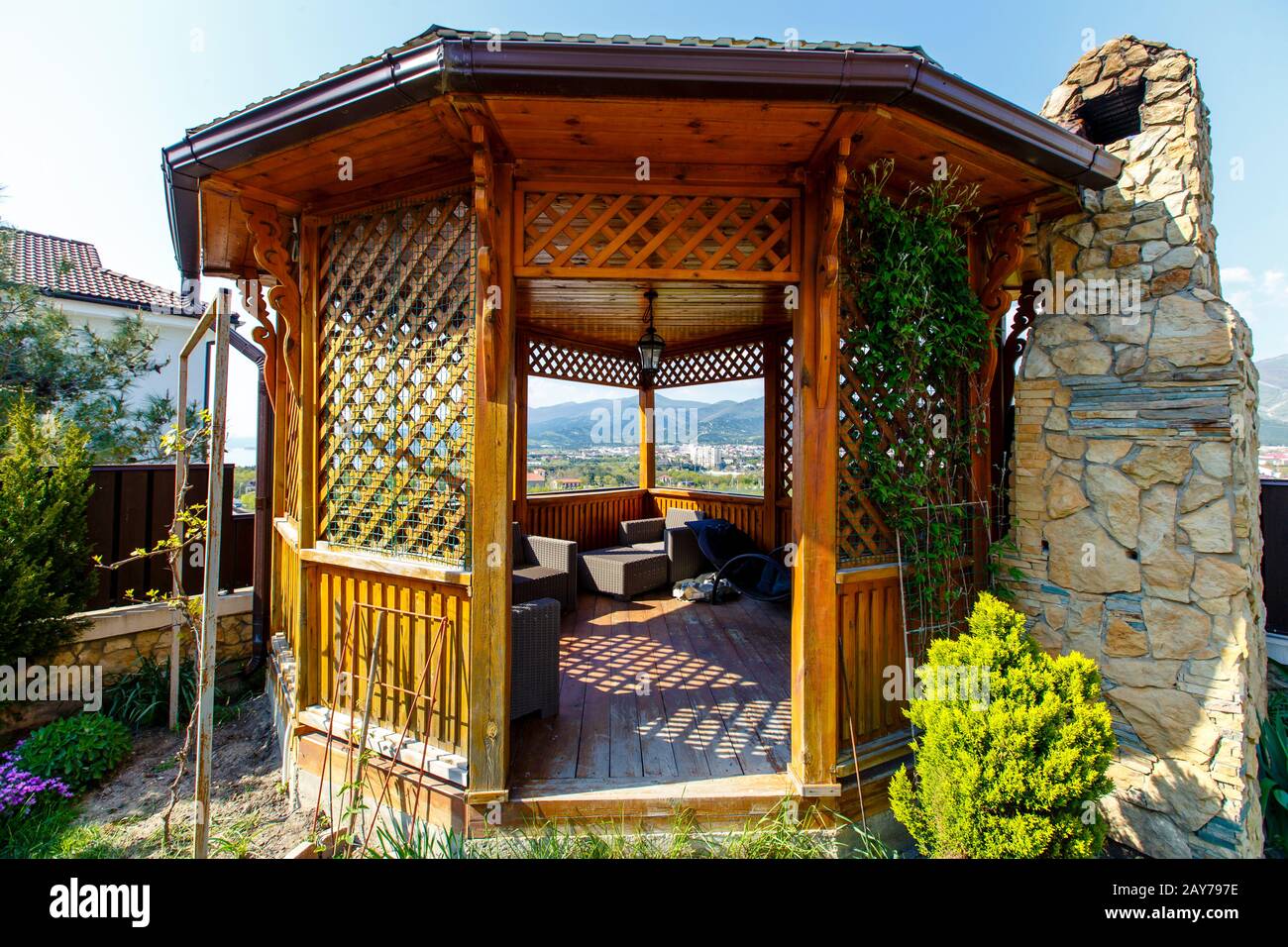 Un gazebo in legno con una stufa a barbecue in pietra nel cortile del cottage. Gazebo accanto alla recinzione nell'angolo del cortile. C'è un prato verde Foto Stock Un gazebo in legno con una stufa a barbecue in pietra nel cortile del cottage. Gazebo accanto alla recinzione nell'angolo del cortile. C'è un prato verde Foto Stock
