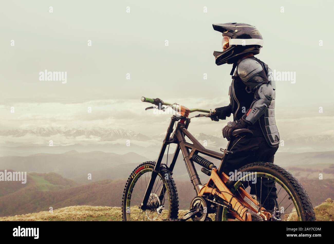 Il pilota nel casco integrale e l'equipaggiamento protettivo completo sulla moto mtb si trova su una roccia sullo sfondo di un RID Foto Stock