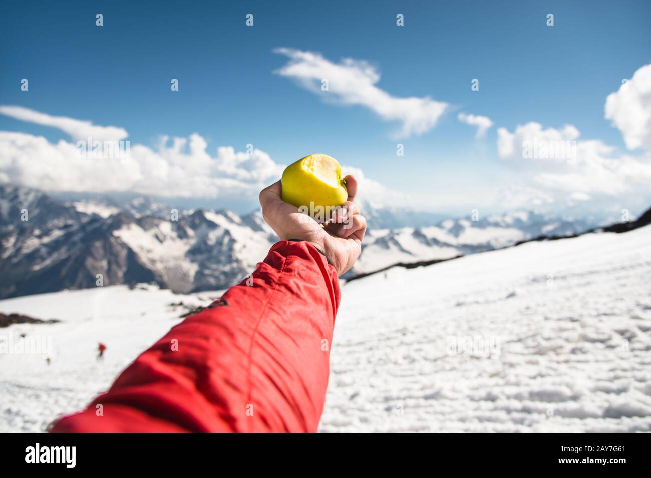 Una mano dell'uomo tiene una mela con un morso sullo sfondo di montagne innevate e neve sotto il piede. Foto Stock