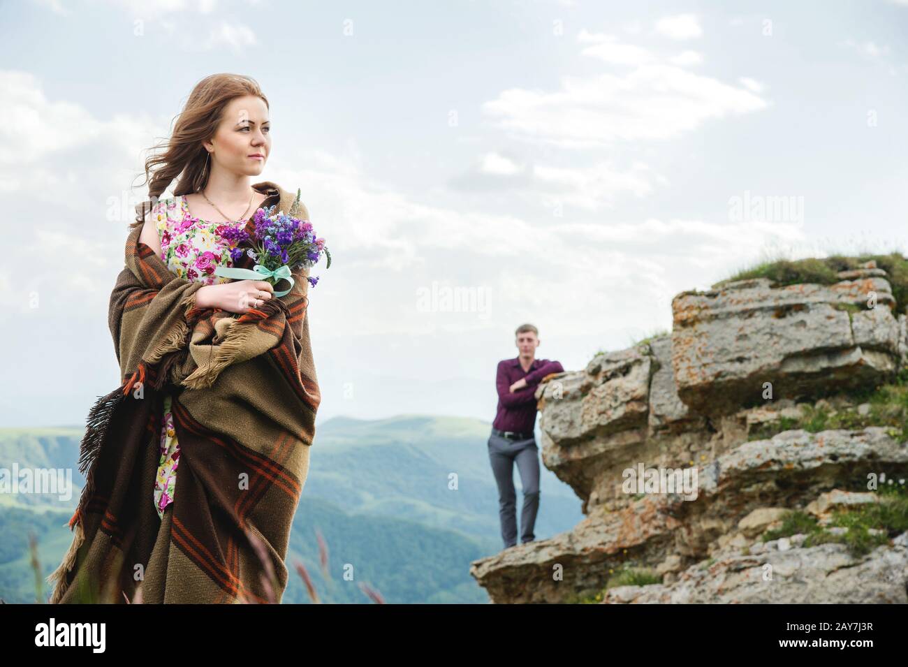 Ritratto di una giovane sposa in un abito colorato con un bouquet di fiori selvatici nella natura in piedi sullo sfondo del suo boyf Foto Stock