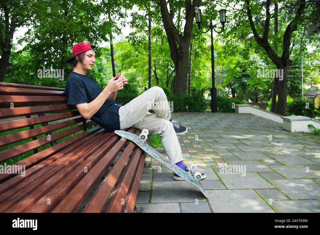 Lo skater da hippster a pelo lungo in un cappello si siede su una panchina e gira su una spinner Foto Stock