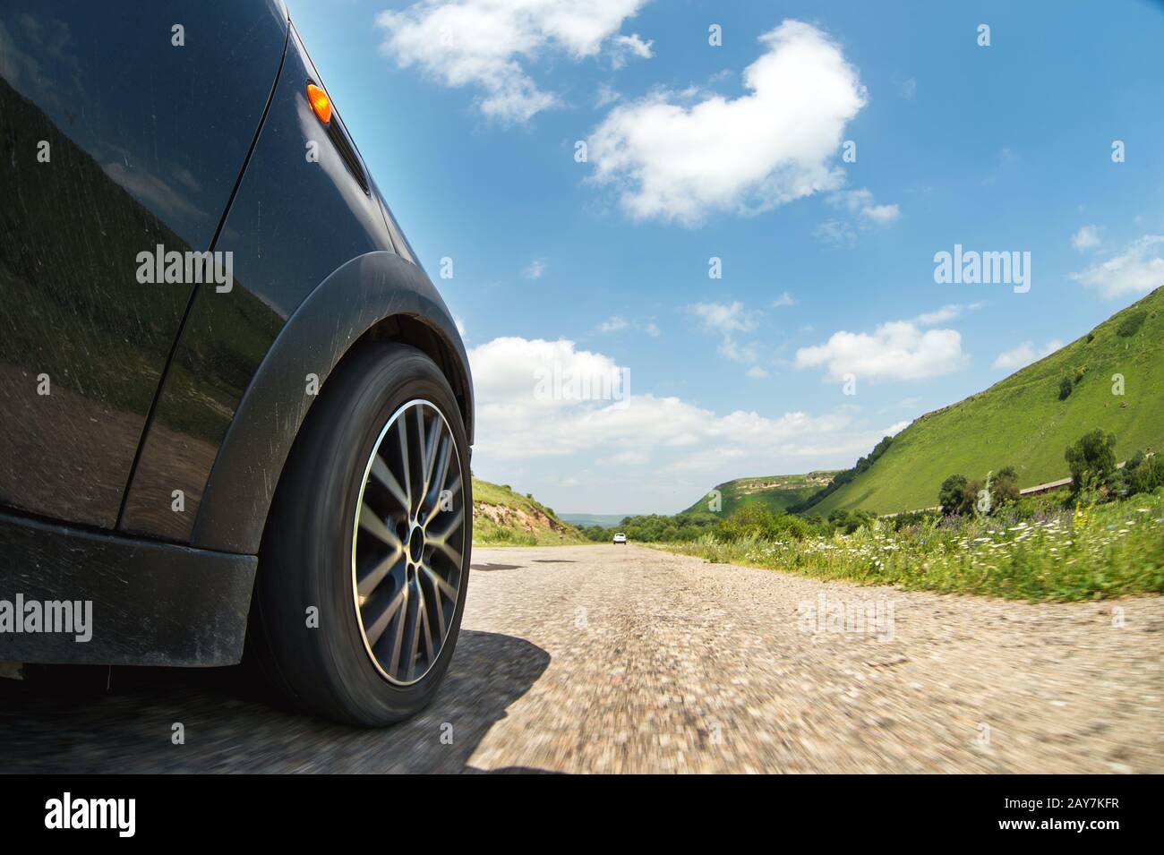 Un primo piano del lato della vettura e una ruota girevole che corre lungo l'asfalto ad alta velocità Foto Stock