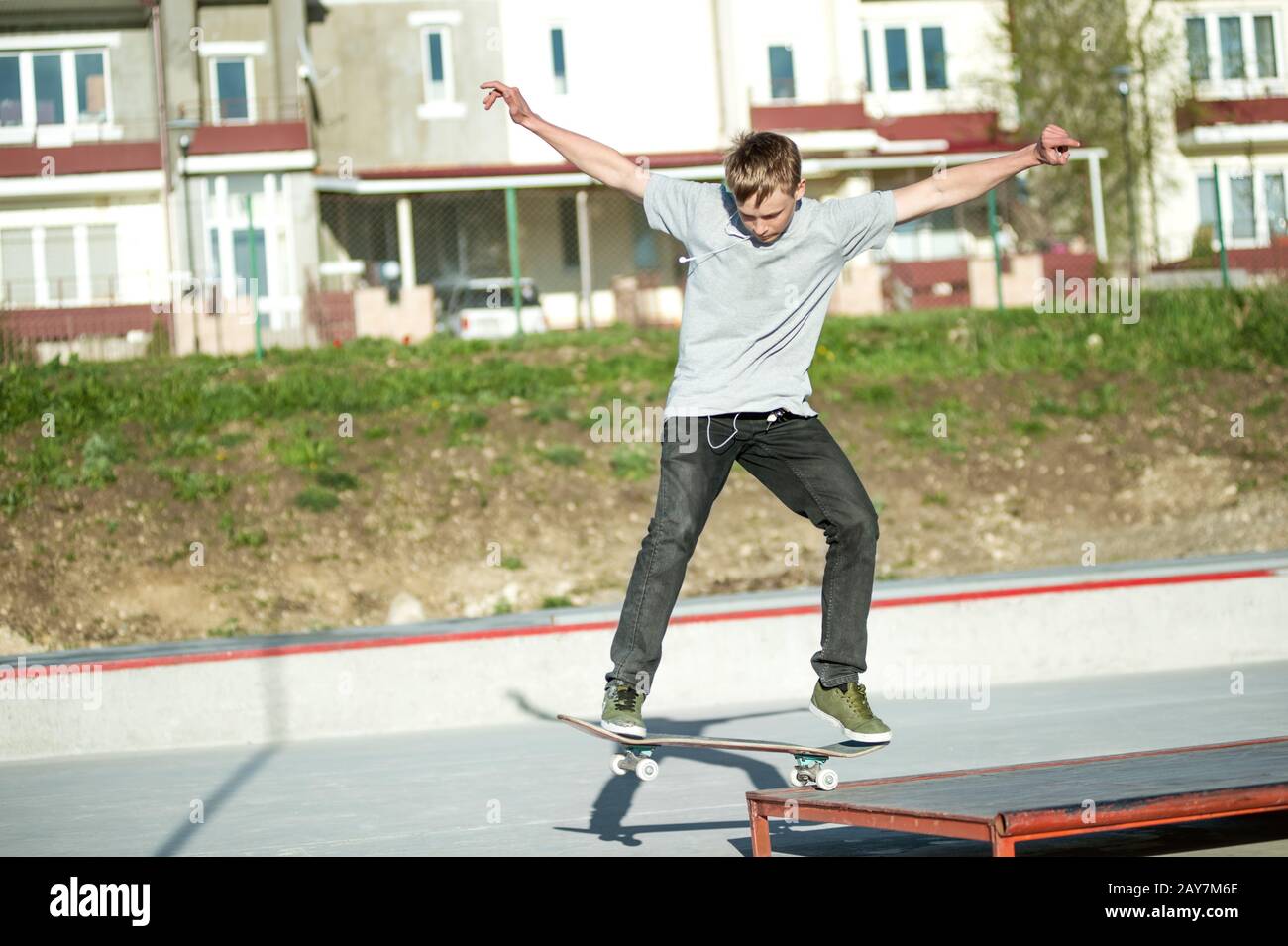 Un giovane ragazzo scivola su uno skateboard in un manuale su uno skatepark sullo sfondo della casa Foto Stock