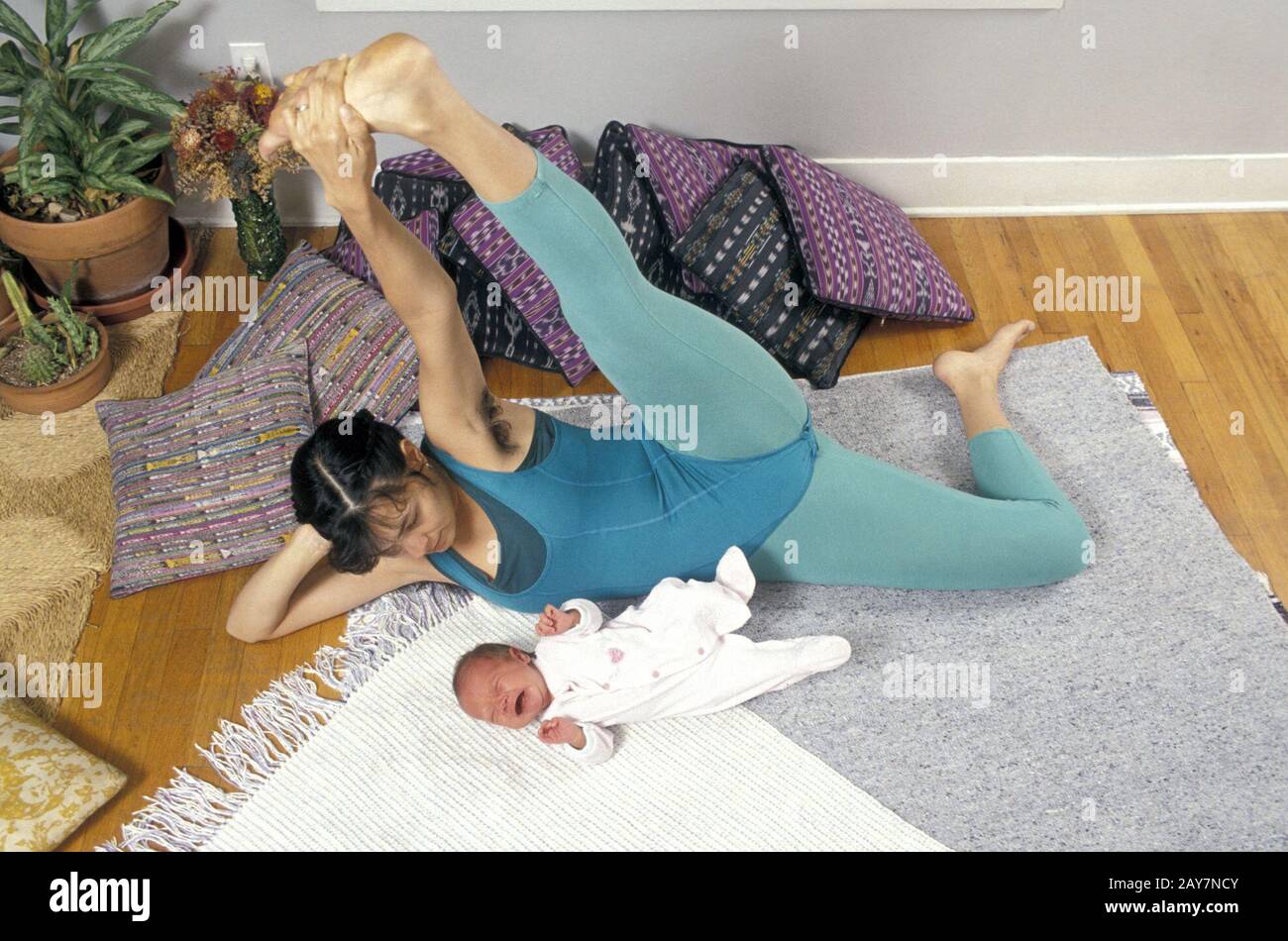 L'istruttore di yoga si allunga mentre fa Hatha Yoga con il suo bambino di 4 settimane al suo fianco. ©Bob Daemmrich Foto Stock