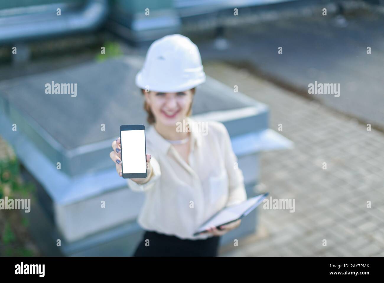 Attraente donna d'affari in blusa bianca, orologio, casco e gonna nera stand sul tetto e mostrare smartphone vuoto Foto Stock