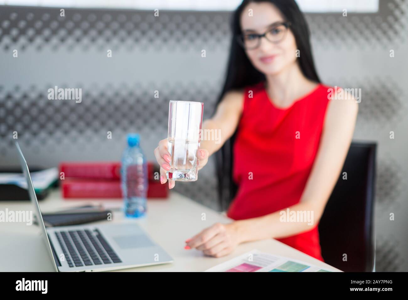 Bella, giovane donna d'affari in abito rosso e occhiali sedersi al tavolo e lavoro Foto Stock