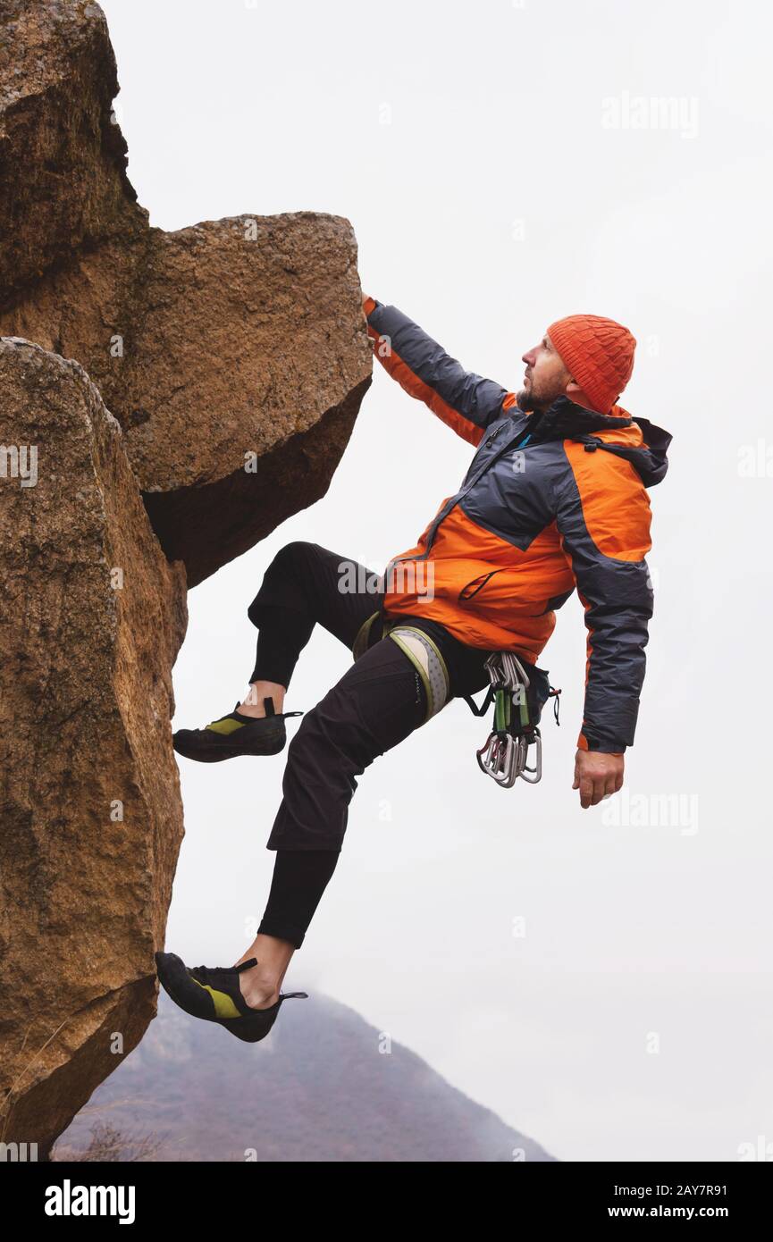 Hippster - scalatore sospeso da una parte su una roccia sullo sfondo delle montagne caucasiche nel tardo autunno. Foto Stock