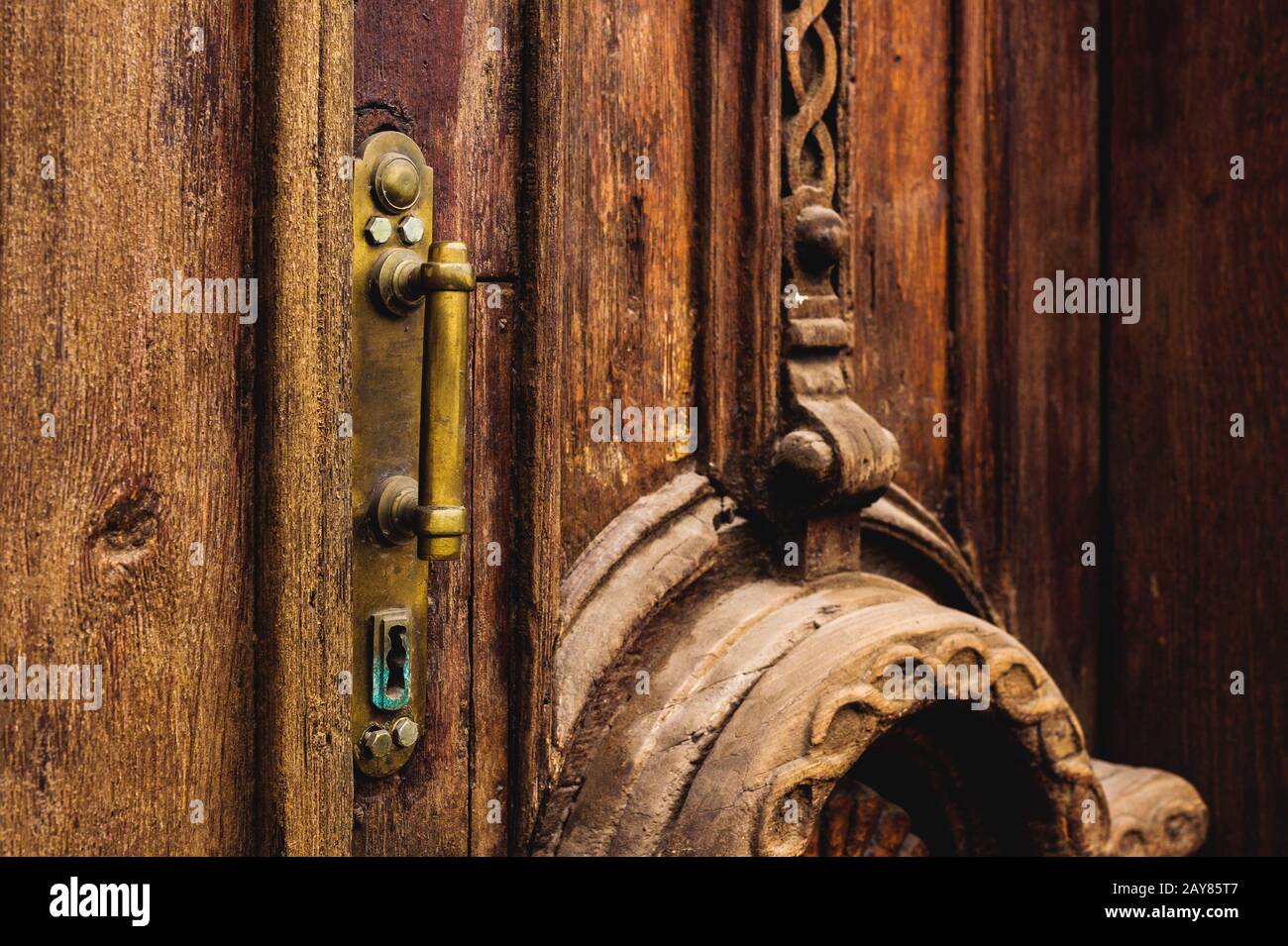Sfondo vintage. Vecchia maniglia in ottone con elementi di una porta in legno intagliato decorata con massiccio tessuto in legno simulante Foto Stock