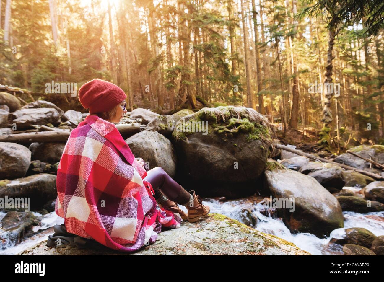 Una bella ragazza hippster con un plaid sulle sue spalle in un cappello e un maglione giallo e bicchieri con una tazza di caffè in lei Foto Stock