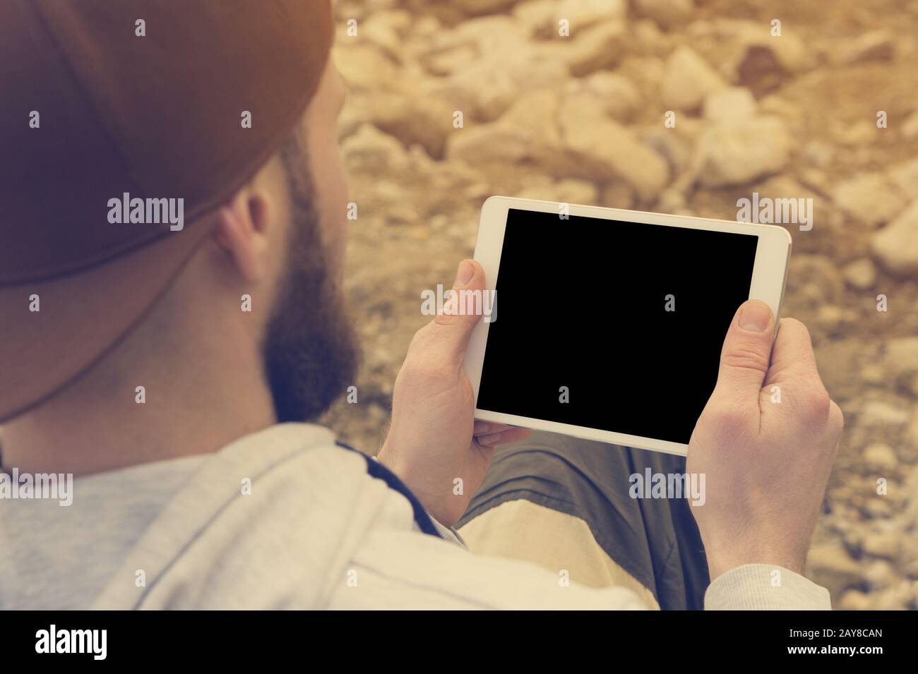 Il primo piano di un'orda in un cappuccio marrone all'aperto contiene un tablet pc bianco nelle sue mani. Un uomo bearded guarda la compressa. OTS Foto Stock