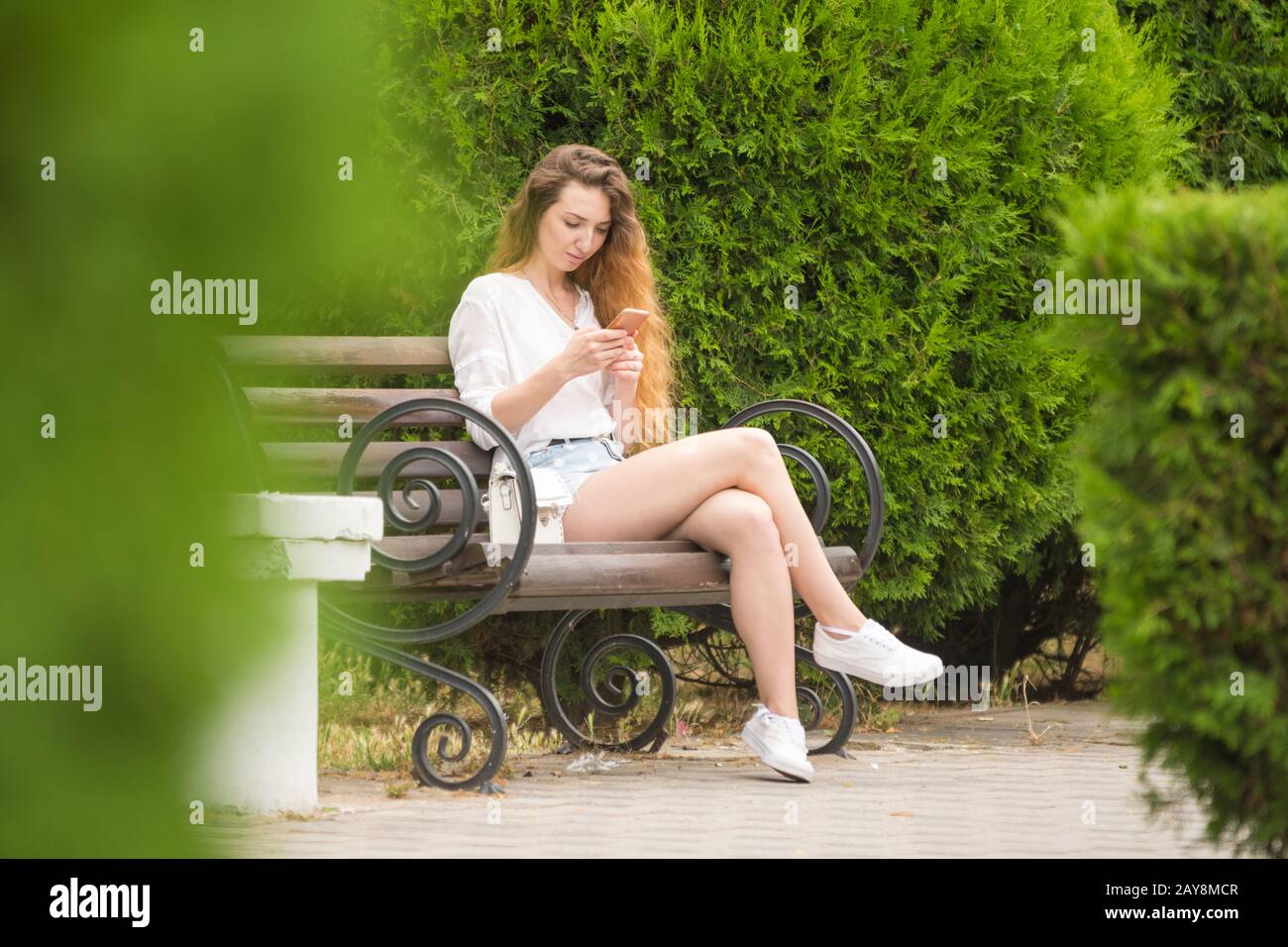 Ragazza giovane comunica in reti sociali seduta su una panchina nel parco Foto Stock