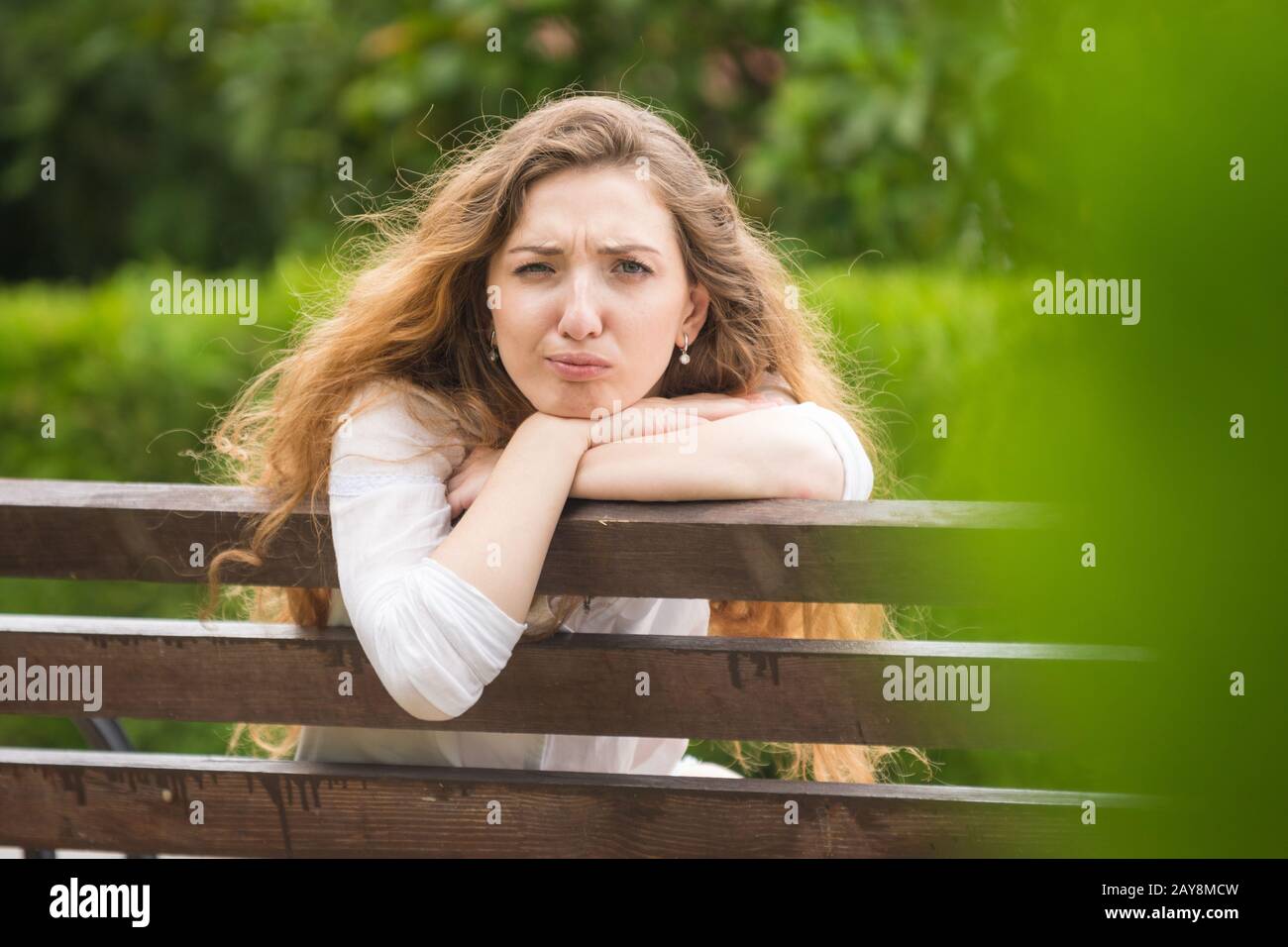 Una giovane ragazza seduta su una panchina si voltò e guardò ridicolmente nel telaio Foto Stock