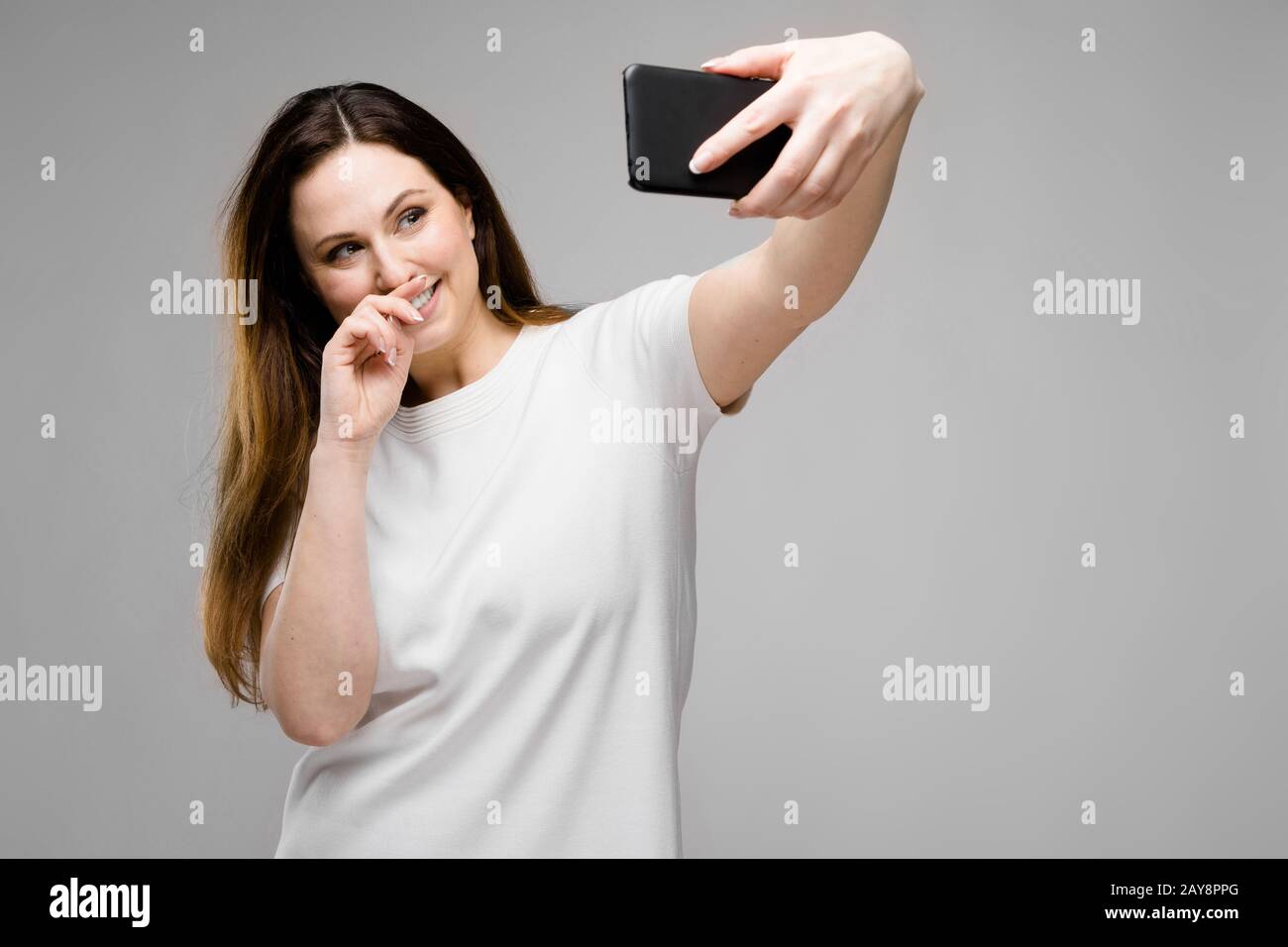 Emotional sorridendo felice plus modello dimensioni in piedi in studio cercando nella fotocamera rendendo selfie Foto Stock