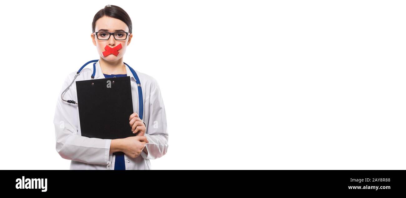 Giovane donna medico con stetoscopio negli appunti di contenimento nelle sue mani con labbra con nastro in divisa bianca su sfondo bianco Foto Stock