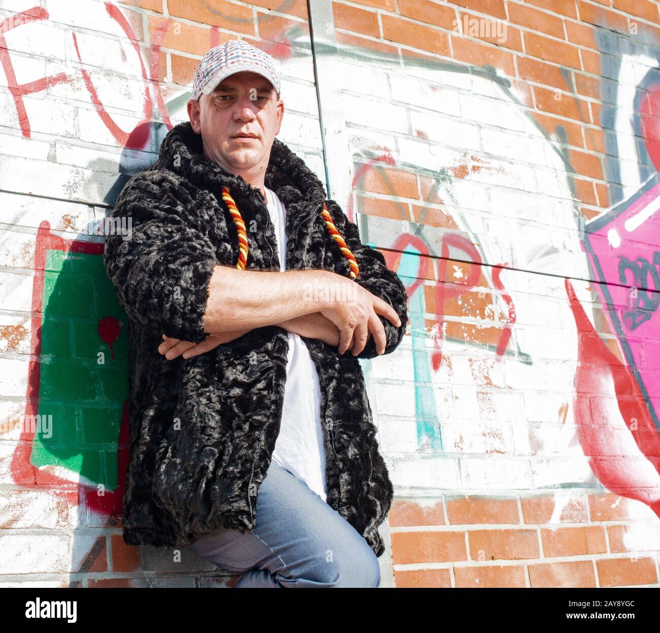 Posa di un modello uomo in pelliccia sintetica giacca di fronte a una parete graffiti Foto Stock