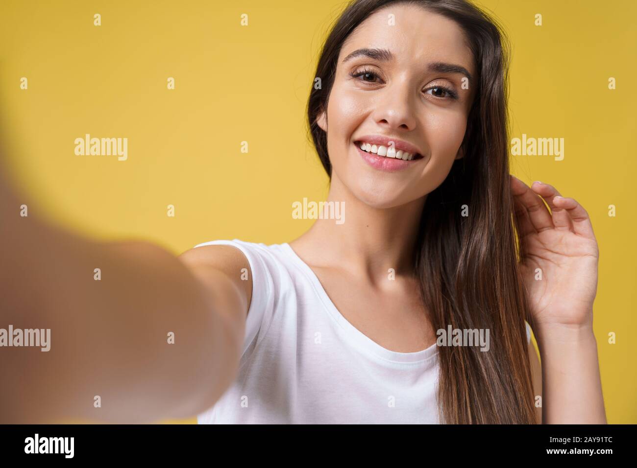 Piacevole ragazza attraente che fa selfie in studio e ridendo. Giovane donna dall'aspetto buono con capelli marroni che scattano l'immagine dell'erigella Foto Stock