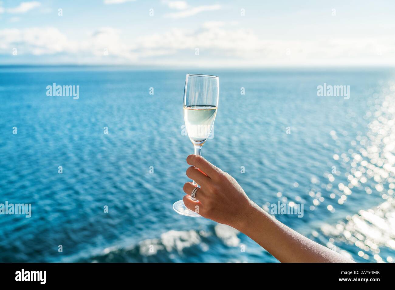 Bicchiere di champagne da donna che torreda sullo sfondo dell'oceano a bordo di una nave da crociera di lusso al tramonto. Vacanza di viaggio per luna di miele, signora che tiene flauto indossare l'anello di nozze. Foto Stock