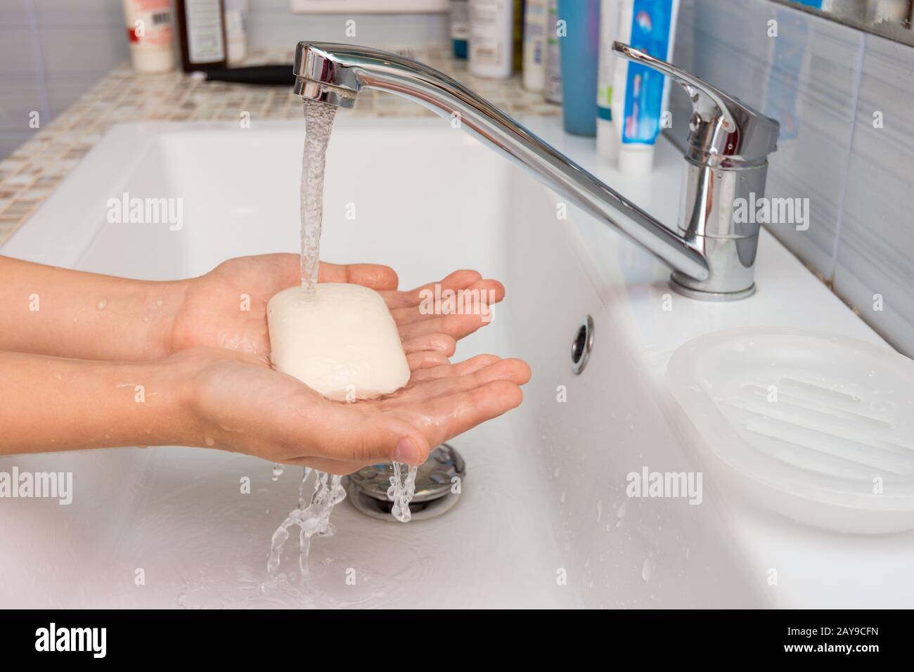 Il bambino tiene in mano il sapone in cui scorre l'acqua dal miscelatore Foto Stock