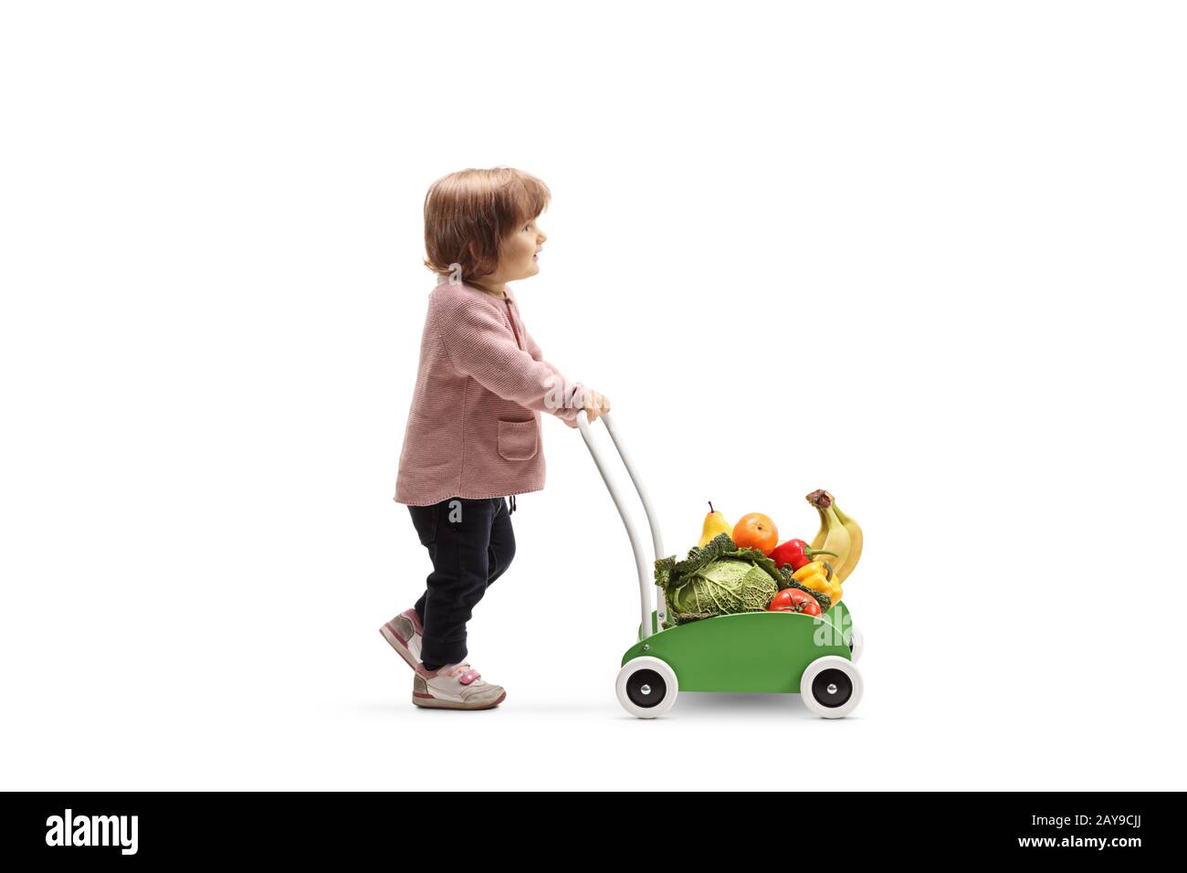 Full lunghezza profilo shot di bambino ragazza camminare e spingere un carrello giocattolo con frutta e verdura isolato su sfondo bianco Foto Stock