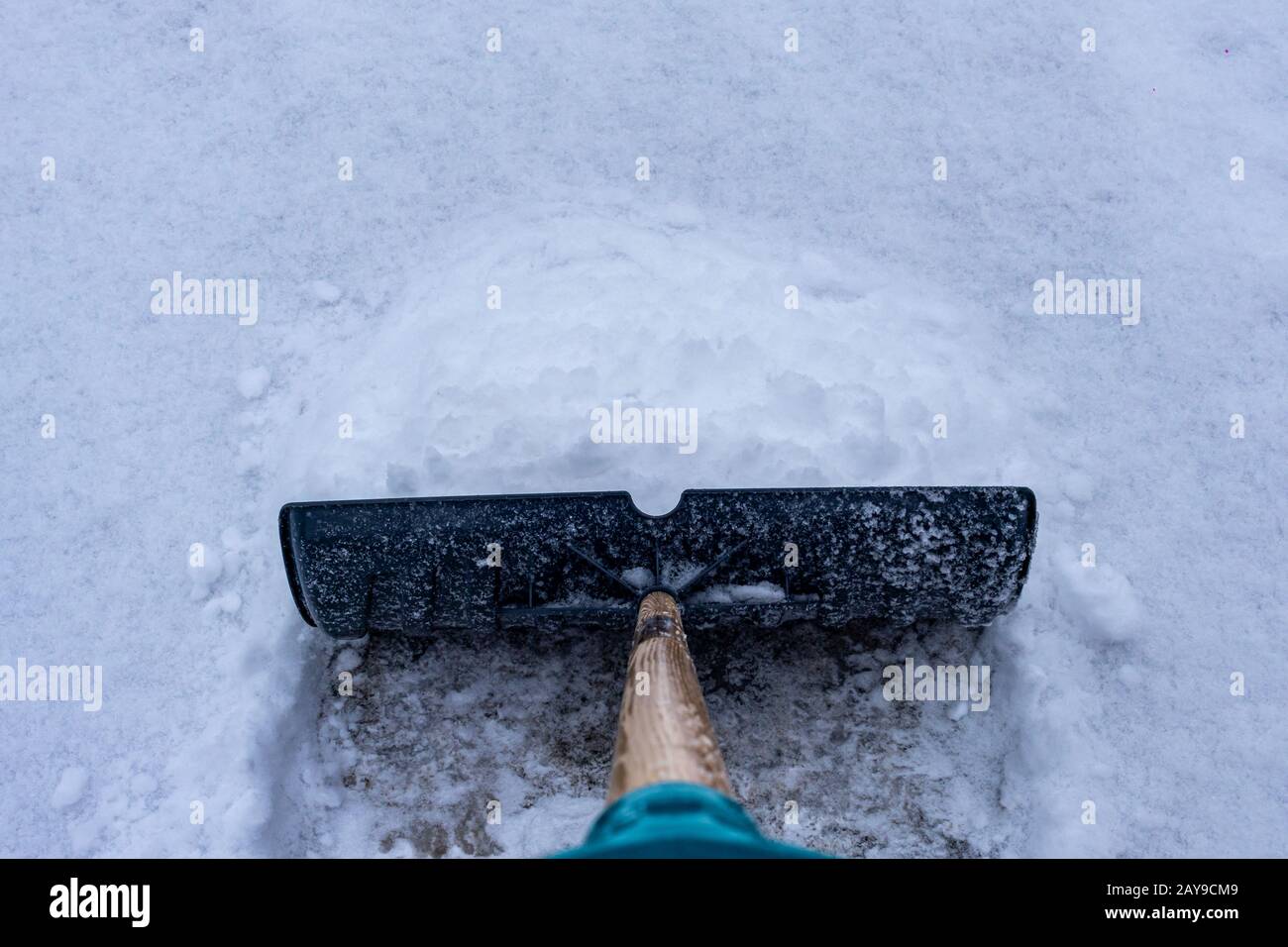 Si vede una pala da neve che spinge la neve lungo un vialetto d'accesso dal punto di vista di qualcuno che sta spalando la propria corsia dopo una nevicata invernale. Foto Stock