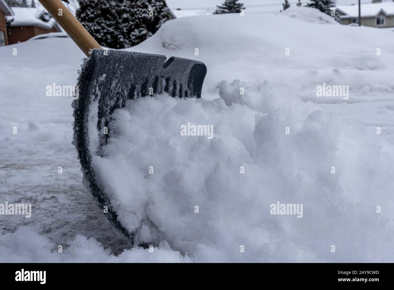 Una pala da neve sta spingendo la neve lungo un vialetto suburbano in inverno. Visto dal livello del suolo, il fondo della pala si vede scavando il fr Foto Stock