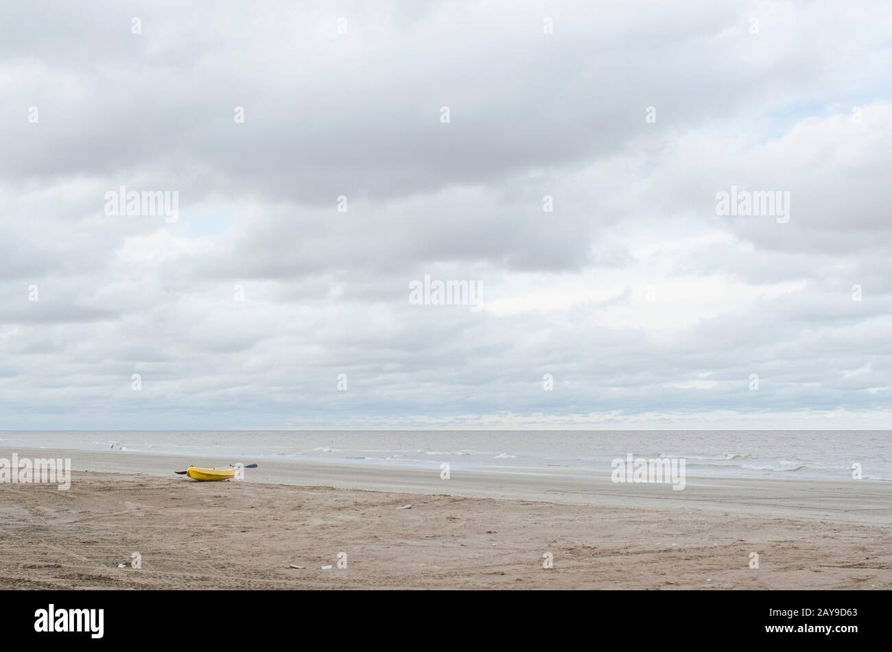 Paesaggio di spiaggia senza persone, un kayak giallo nella sabbia, un mare calmo e un cielo nuvoloso, a Punta Rasa, provincia di Buenos Aires, Argentina Foto Stock