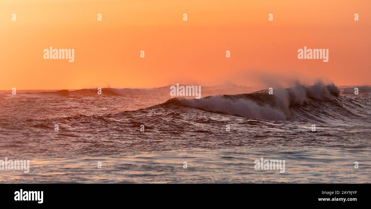 onde che si rompono al tramonto creando spruzzi Foto Stock