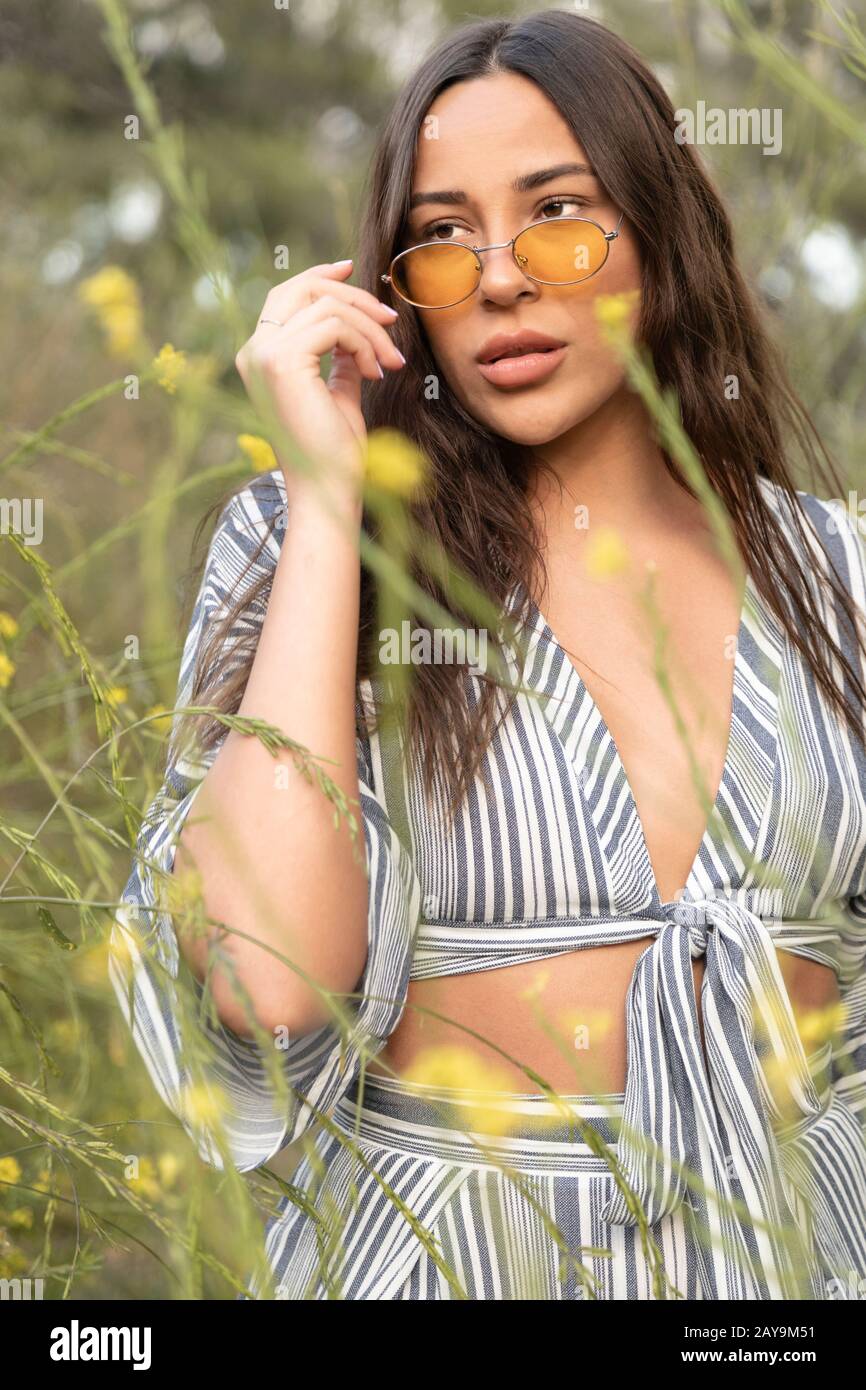 Donna Latina elegante con occhiali da sole in campi di fiori Foto Stock