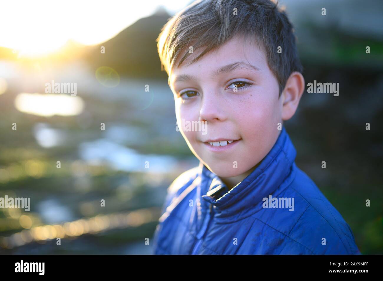 Ritratto di un ragazzo con cappotto blu sorridente all'esterno al tramonto Foto Stock