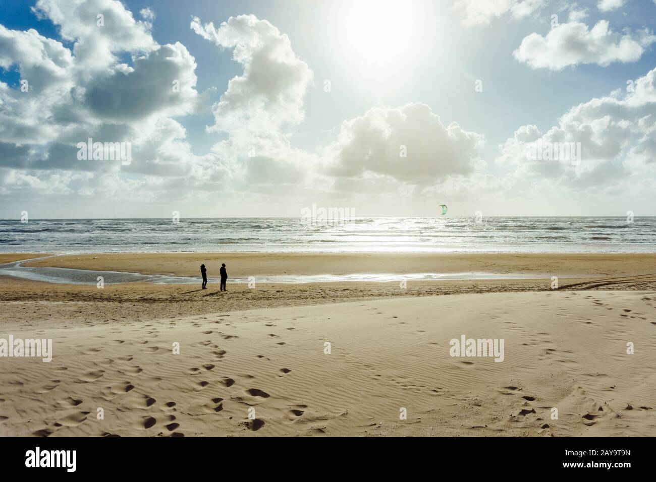 La gente alla vista panoramica del mare pianeggiante di fango che guarda un kitesurfer Foto Stock