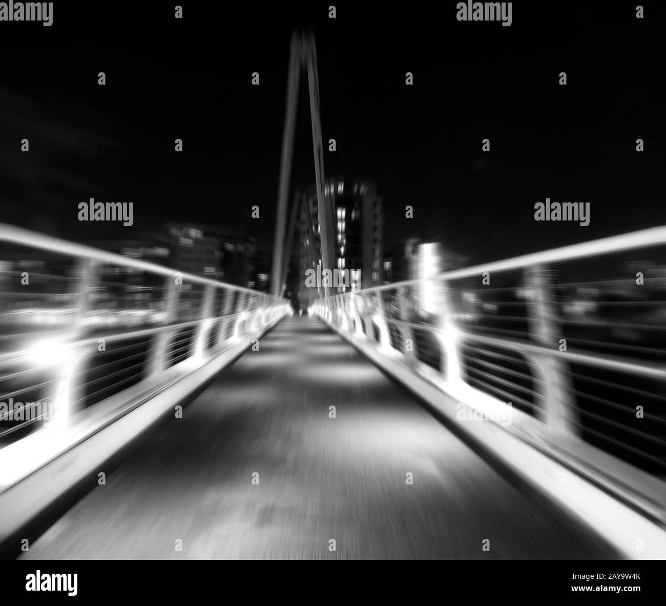 zoom monocromatico sfocare l'immagine di un ponte pedonale in un ambiente urbano di notte Foto Stock
