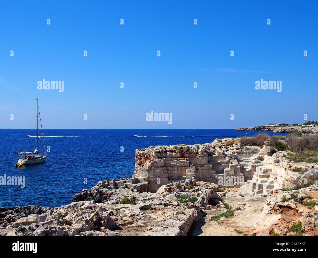 Una scena costiera con uno yacht in un mare mediterraneo illuminato dal sole blu vicino ciutadella menorca Foto Stock
