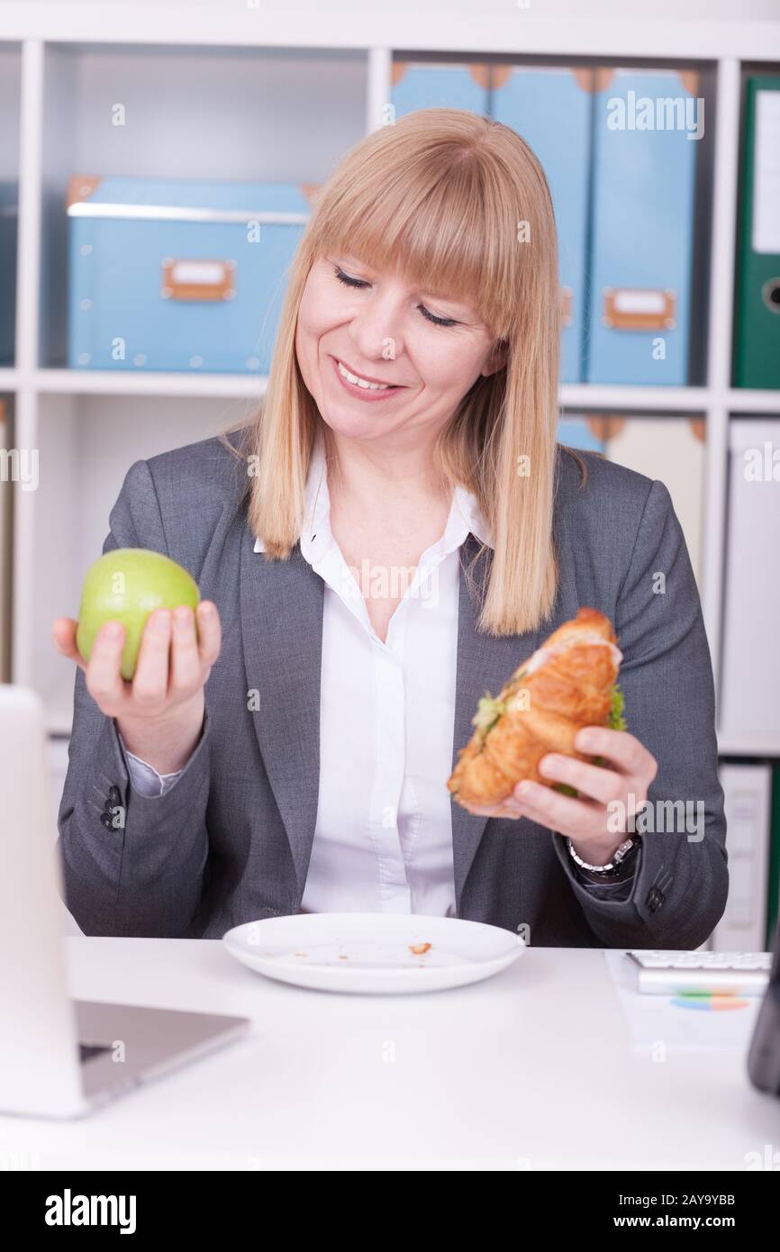 Donna in ufficio a pranzo. Concetto per salutare o alimenti dannosi per la salute sul lavoro. Foto Stock