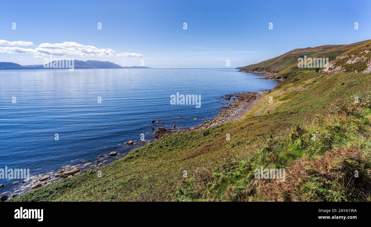 Linea rocciosa costale e montagne a distanza con cielo e mare blu Foto Stock