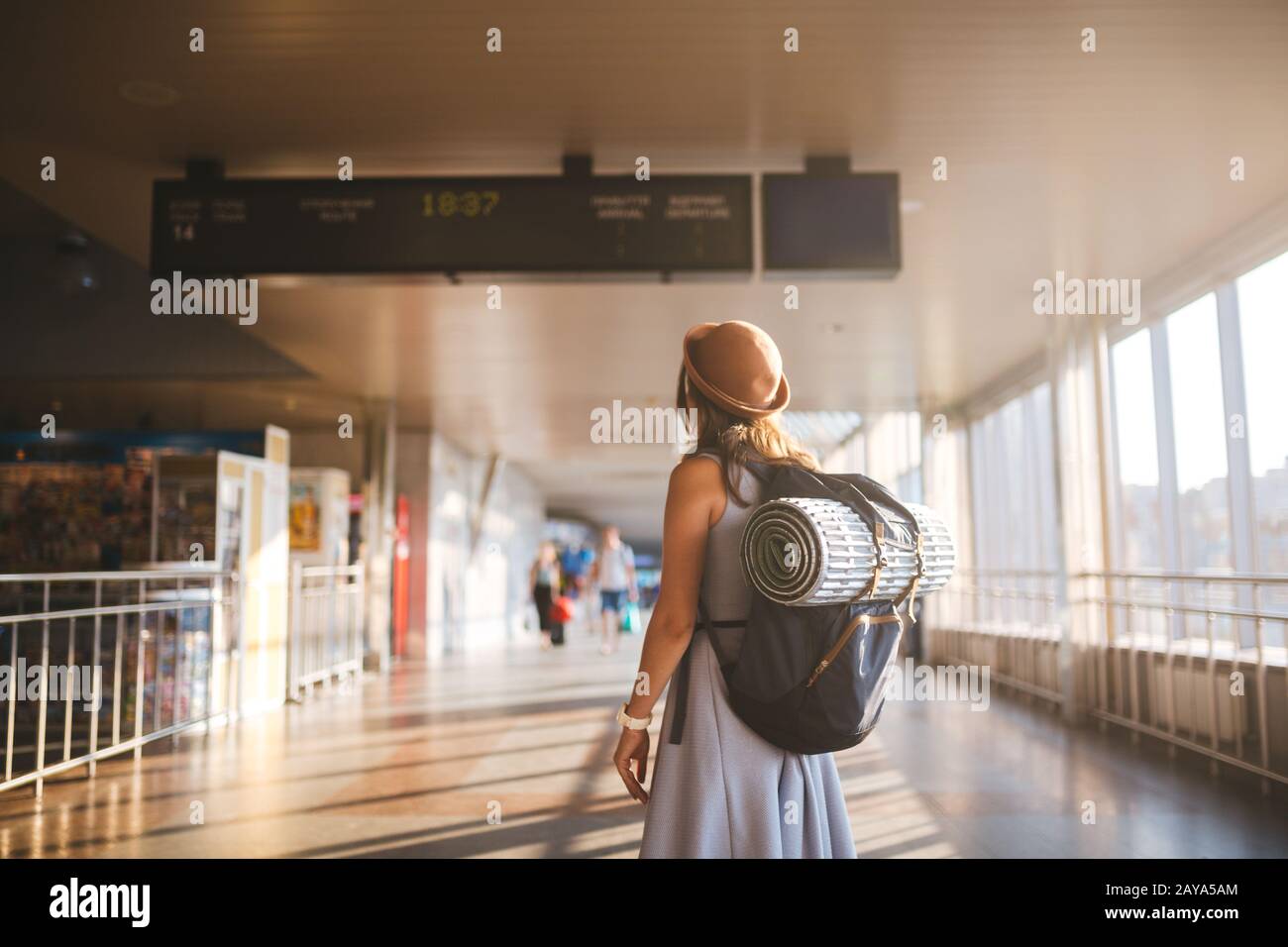 Trasporto pubblico a tema. Giovane donna in piedi con schiena in abito e cappello dietro zaino e attrezzature da campeggio per il sonno Foto Stock