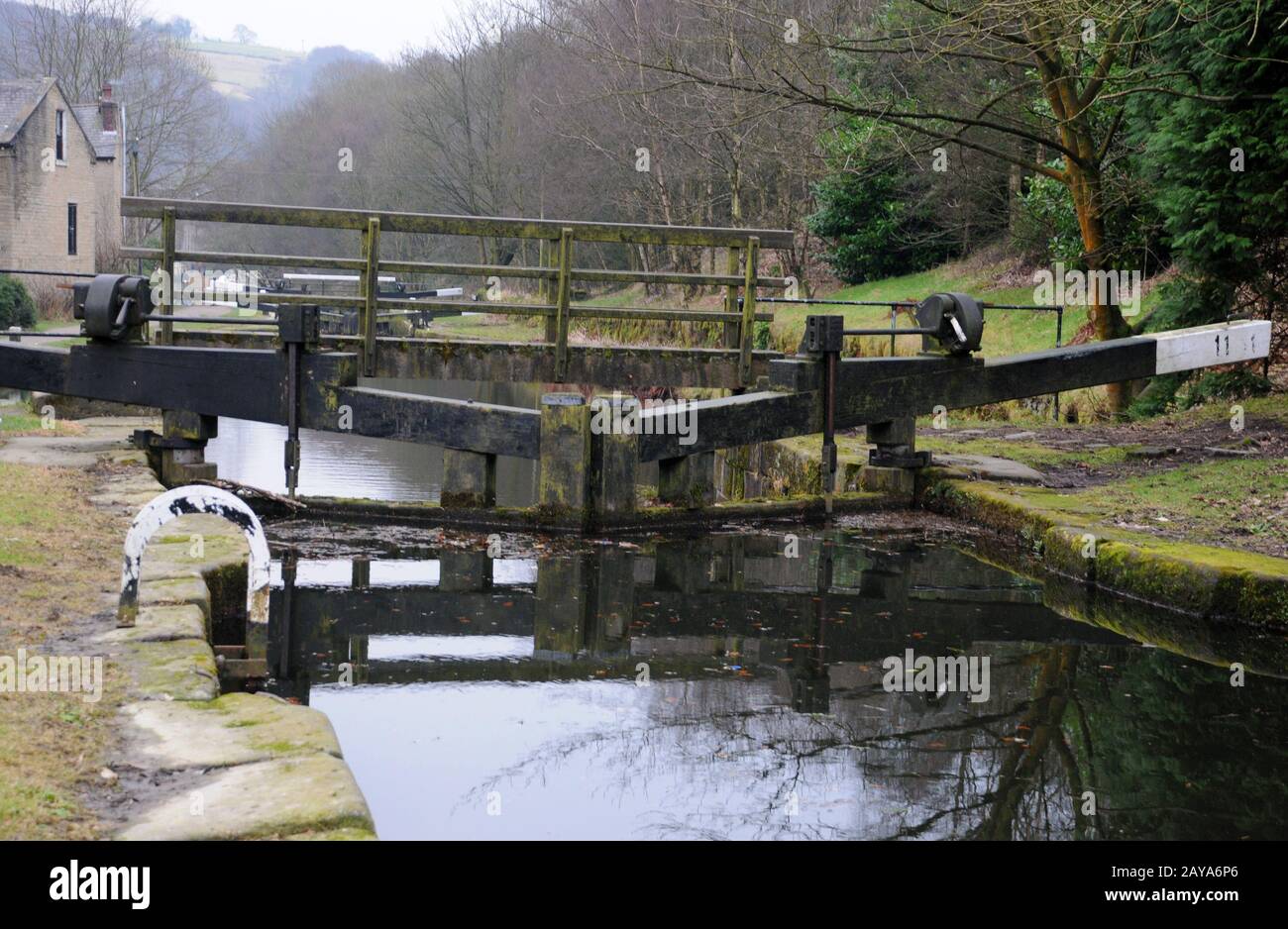 set di porte a serratura su un canale con passerella in legno con acqua scura che riflette gli alberi e il paesaggio vicino al ponte hebden Foto Stock