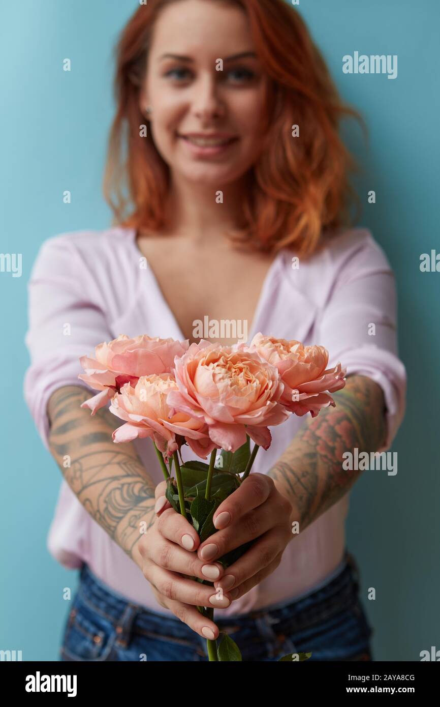 Un sorridente ragazza con un tatuaggio offre un bouquet di rose rosa intorno a uno sfondo blu con copia spazio. La festa della mamma regalo Foto Stock