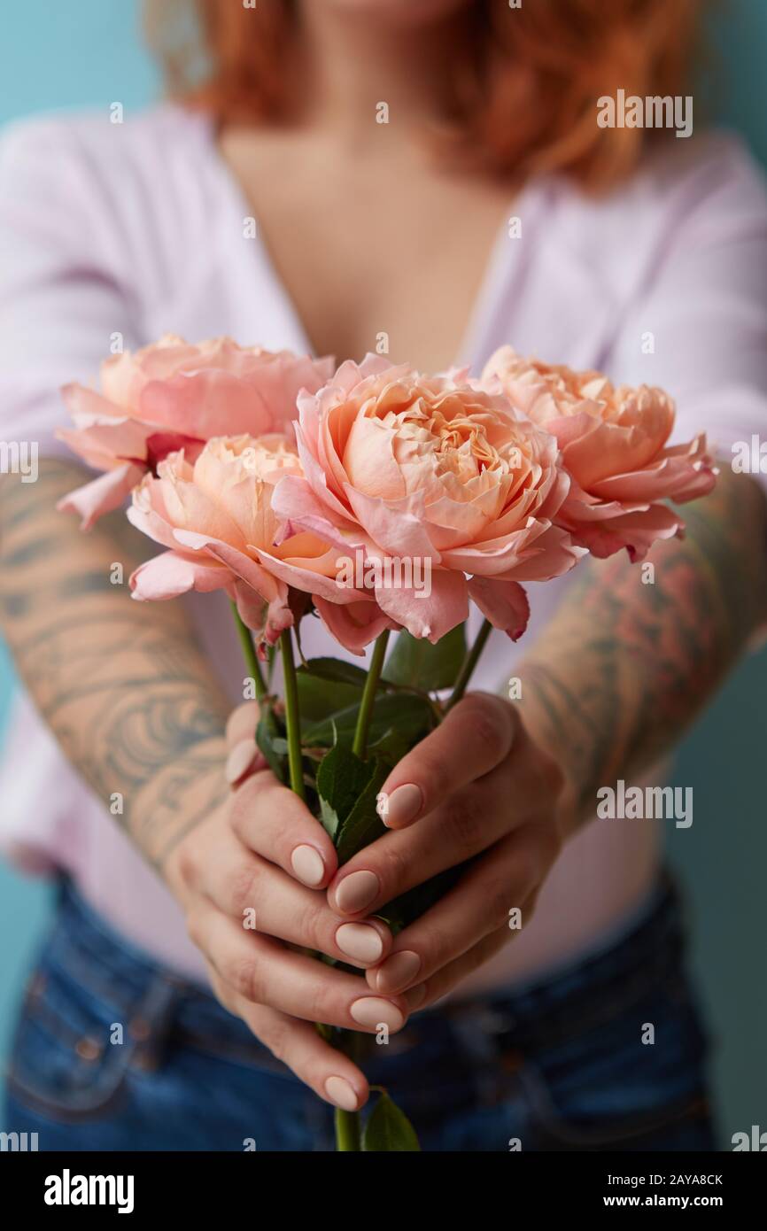 Una donna con un tatuaggio holding delicate rose rosa nelle sue mani su uno sfondo blu con copia spazio per il testo. Regalo per le feste Foto Stock