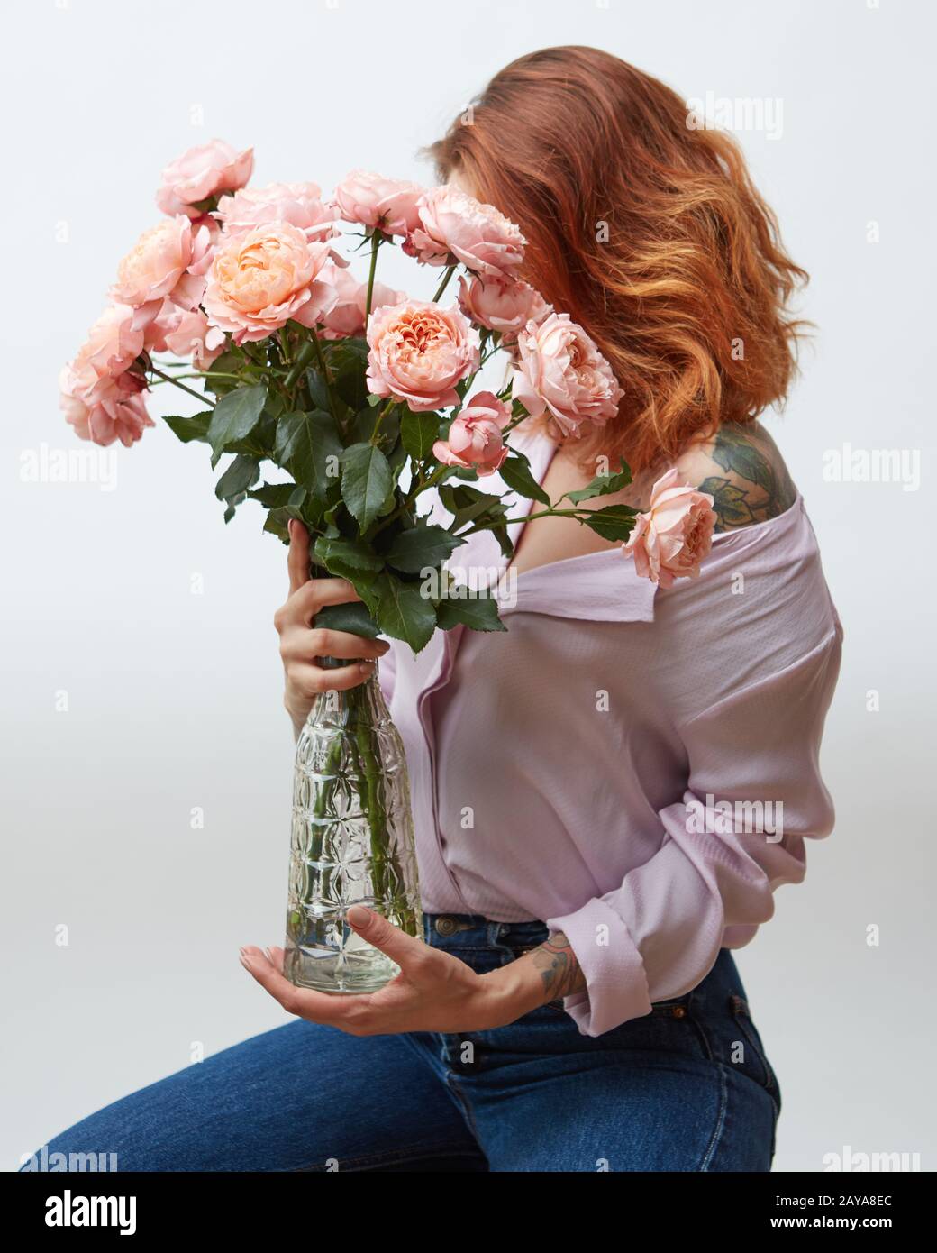 I Capelli rossi ragazza con un tatuaggio e di un bel colore rosa bouquet di rose in un vaso su uno sfondo grigio con copia spazio. La festa della mamma. Foto Stock