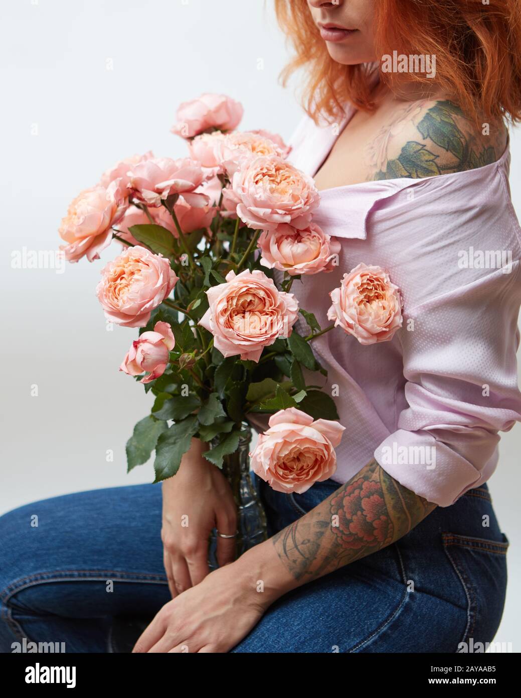 Un bouquet di rose rosa in un vaso può contenere una ragazza con un tatuaggio su uno sfondo grigio con copia spazio. San Valentino Foto Stock