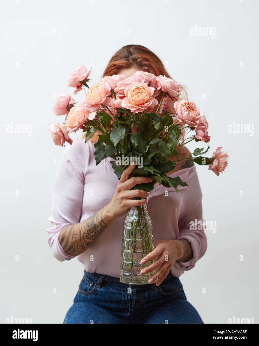 Una donna con un tatuaggio che tiene un grande bouquet di rose rosa in un vaso di vetro intorno ad uno sfondo grigio con spazio di copia. Madre D Foto Stock