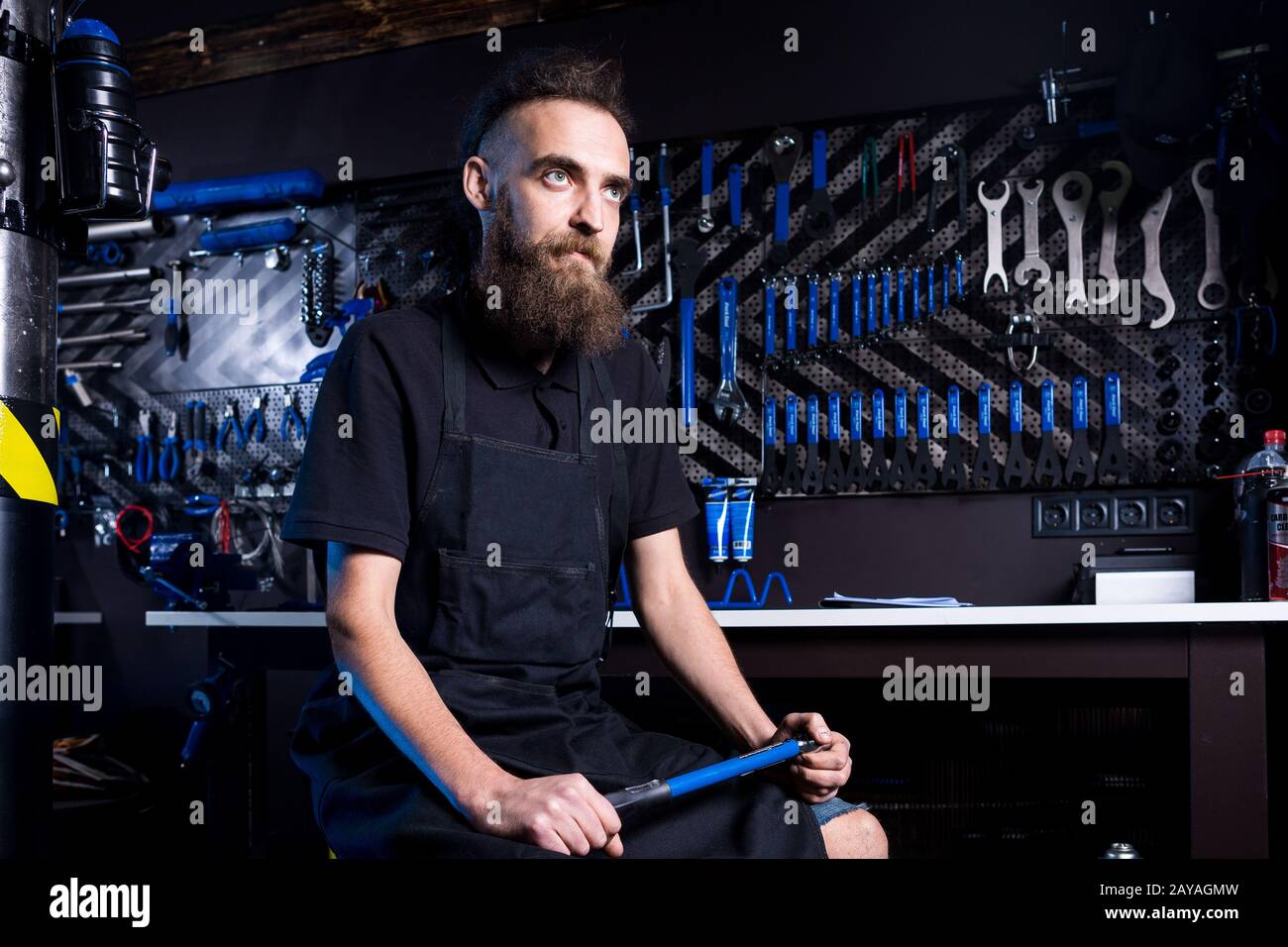 Ritratto di piccola impresa proprietario di giovane uomo con barba. Ragazzo di bicicletta meccanico officina lavoratore seduto con l'attrezzo in mano Foto Stock