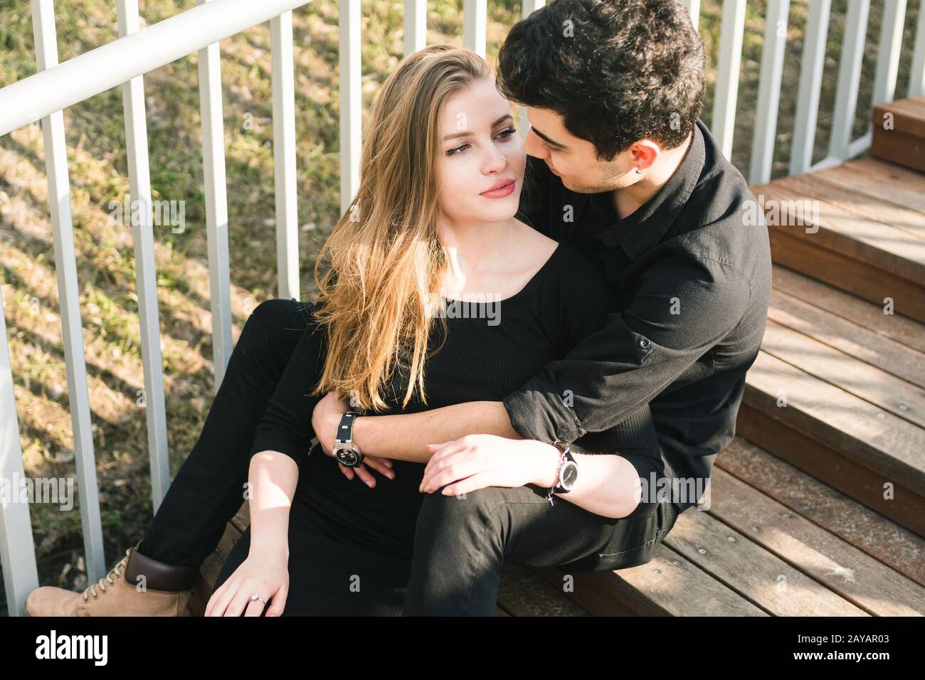Bella giovane coppia multirazziale, coppia studentesca innamorata, sedersi scala in legno in città. Bel bruna turco ragazzo abbraccio Foto Stock