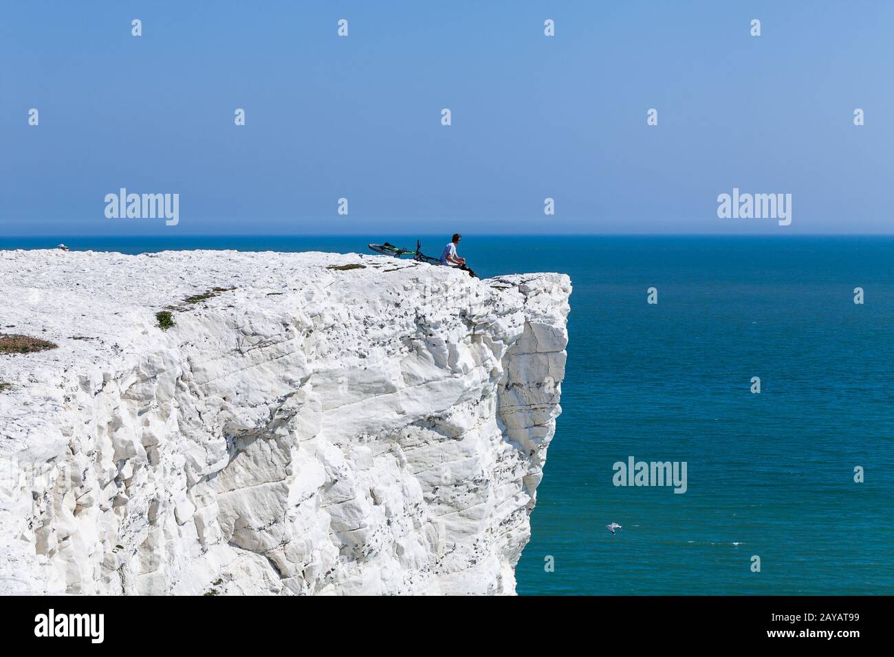 Giovane uomo sulla roccia e godere di una bella vista, maschio seduto sul bordo, bicicletta distesa giù scogliera dal mare. Vacanze estive ricreazione Foto Stock