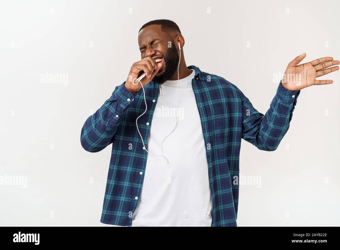 Bello afro-americano in abiti casual è ascoltare musica utilizzando un telefono intelligente e sorridente. Foto Stock