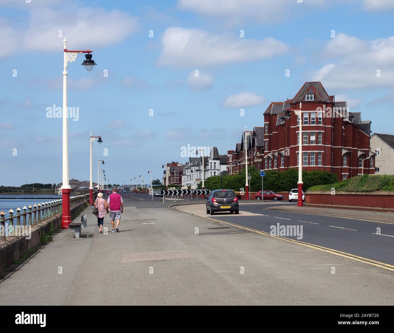 una coppia più anziana che cammina lungo il viale marino di southport merseyside con vecchi edifici alberghieri che costeggiano la strada in un'estate luminosa Foto Stock