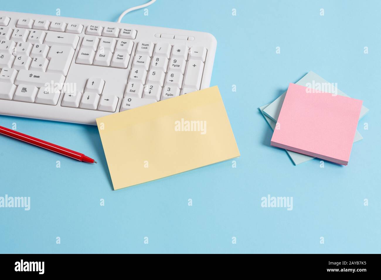 Scrivania blu chiaro con diverse dimensioni di note cartacee vuote, tastiera per computer ed elettrodomestici per ufficio. Spazio vuoto sui promemoria, no Foto Stock