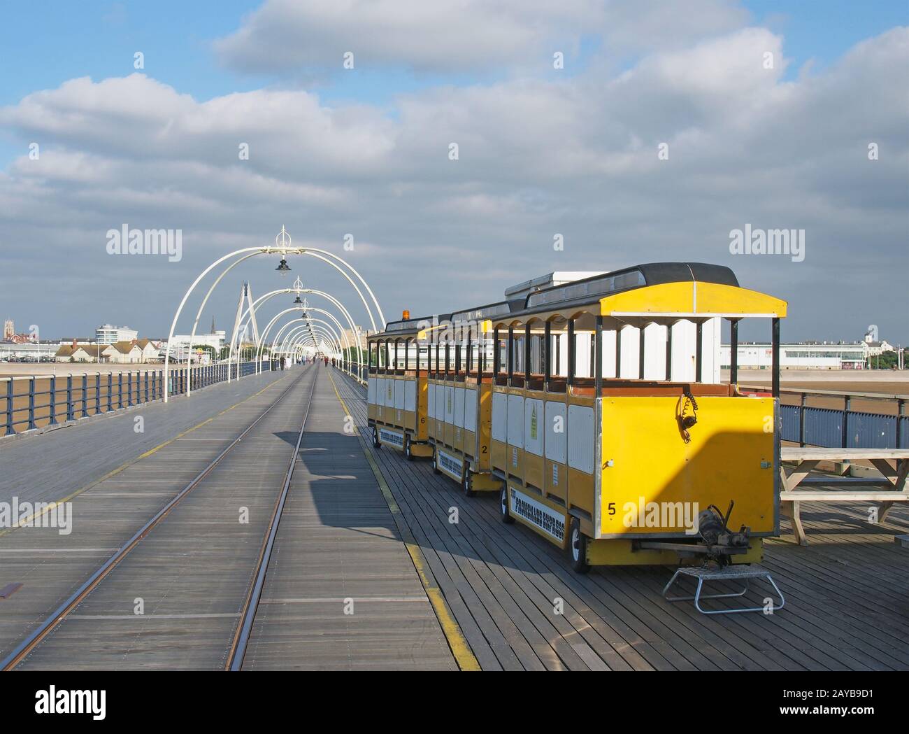 il treno giallo sul molo di southport merseyside in una luminosa giornata estiva con edifici in città contro un cielo blu nuvoloso Foto Stock